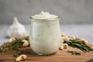 glass jar of rosemary garlic cashew cream on wood cutting board