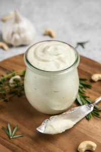 rosemary garlic cashew cream in glass jar with fancy knife on wood cutting board