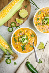 bowls of corn chowder surrounded by corn, limes, and jalapeno pieces