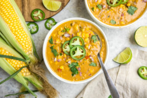bowl of corn chowder topped with jalapenos on grey stone background