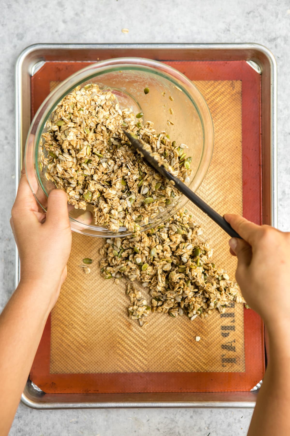 pouring uncooked granola onto baking tray
