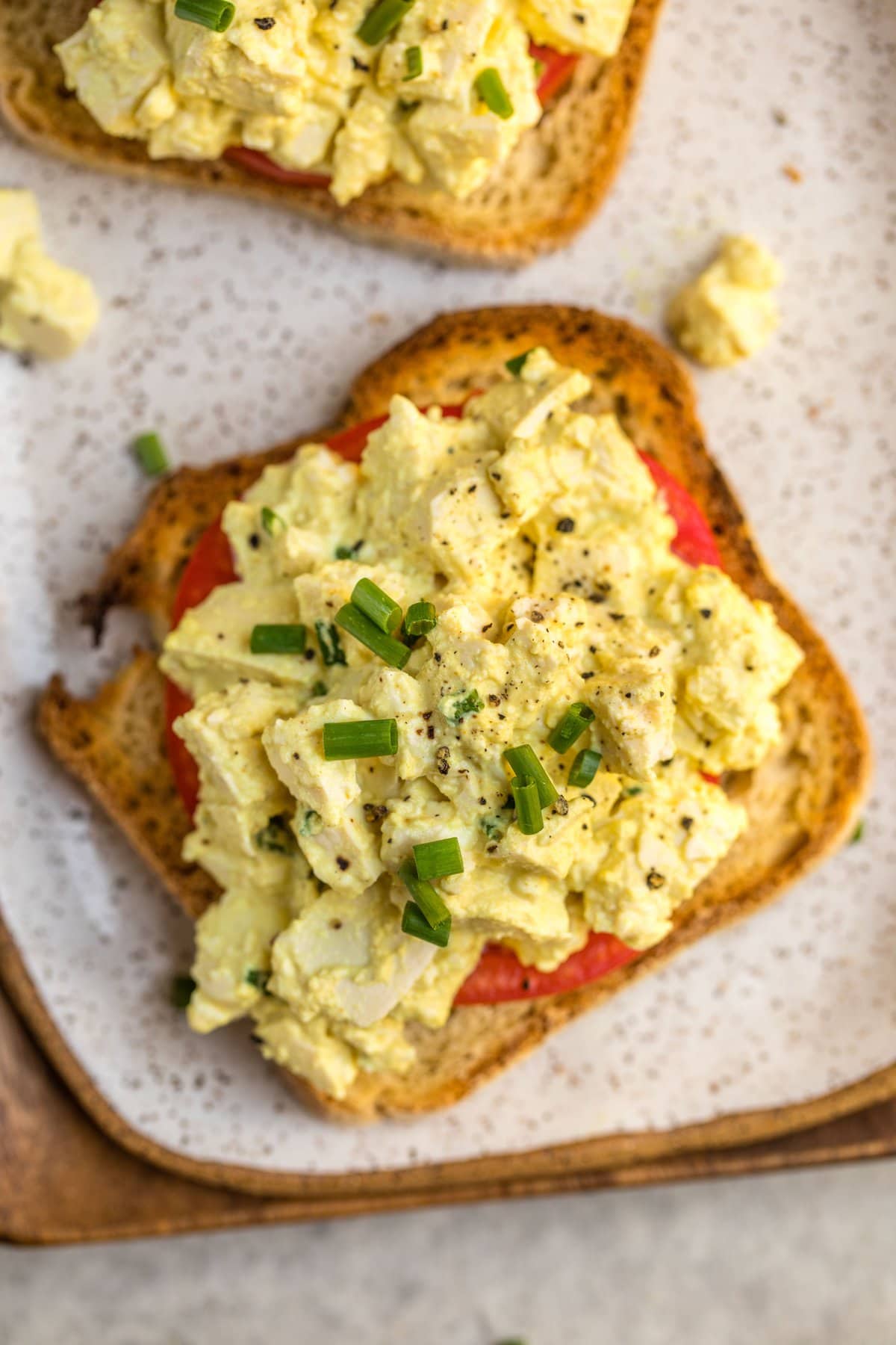vegan egg salad on piece of toasted bread with tomato and fresh chives