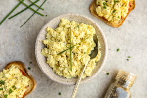 vegan egg salad in large white bowl with fresh chives and black pepper