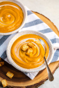 bowls of chipotle sweet potato and pumpkin soup on blue striped towel