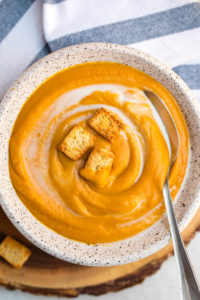 creamy chipotle, sweet potato & pumpkin soup in white speckled bowl and topped with croutons