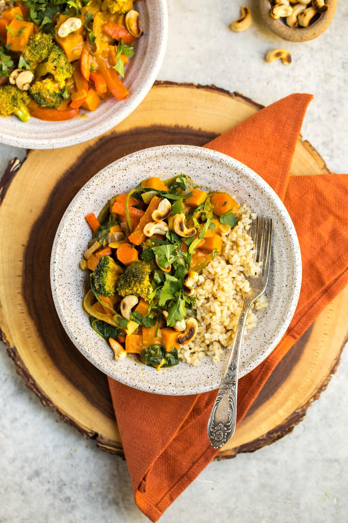 white bowl filled with pumpkin curry and brown rice on top of orange napkin and wood cutting board