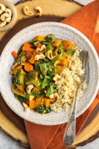 bowl of pumpkin curry served with brown rice, cilantro, and toasted cashews