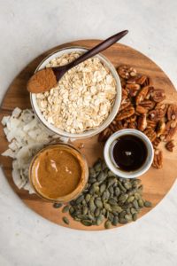 ingredients for pumpkin spice granola on round wood cutting board