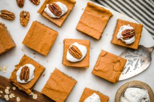 sweet potato pie bars topped with whipped cream and pecans on white marble cutting board