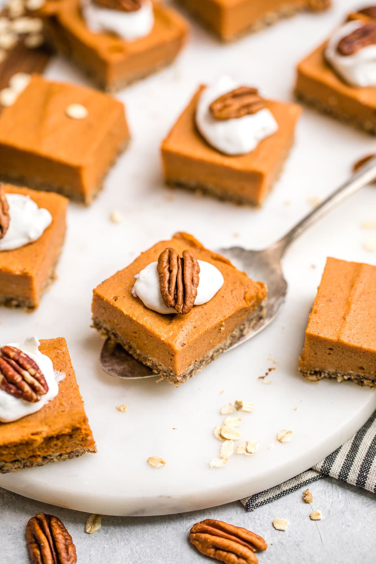 sweet potato pie bars topped with coco whip and a pecan on white serving tray