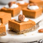 silver spatula holding sweet potato pie bar topped with coco whip and pecans on white cutting board