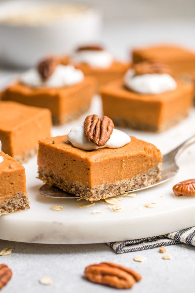 silver spatula holding sweet potato pie bar topped with coco whip and pecans on white cutting board