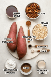 Ingredients for sweet potato pie bars on marble countertop. Clockwise text labels read pecans, rolled oats, vanilla, salt, non-dairy milk, flax, arrowroot powder, sweet potatoes, pumpkin pie spice, and maple syrup