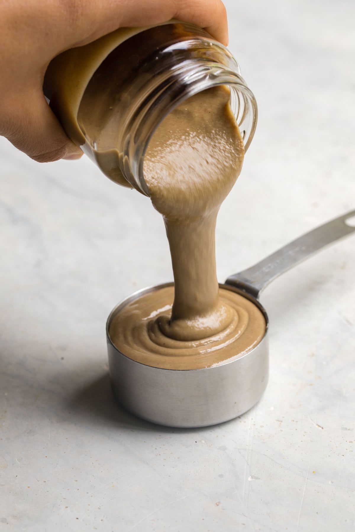 hand pouring tahini into measuring cup