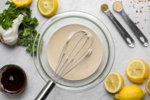 tahini dressing in glass bowl surrounded by various ingredients