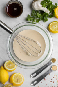 glass bowl of tahini dressing surrounded by optional add-ins on white background