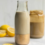 glass bottle filled with tahini dressing on white stone background