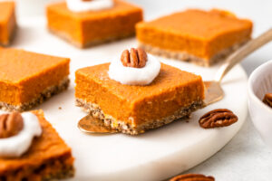 Sweet potato pie bars topped with coconut cream and pecan on marble serving tray