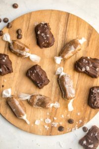 healthy salted caramel bites wrapped in paper and dipped in chocolate on round wood cutting board