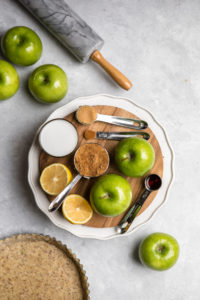 ingredients for salted caramel apple pie filling on round wood cutting board on light gray background