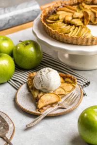 slice of salted caramel apple pie on small white plate topped with scoop of vanilla ice cream