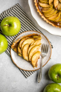 slice of salted caramel apple tart on small white plate with black striped napkin