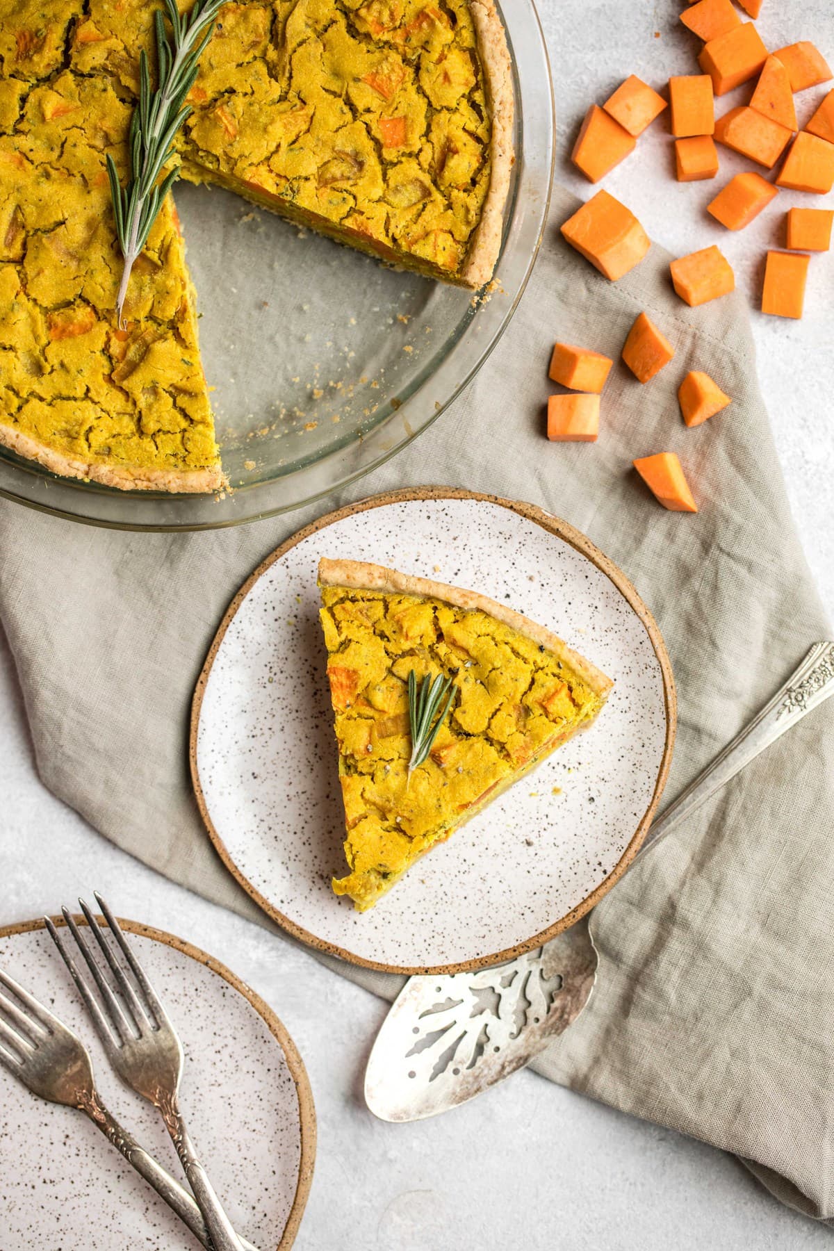 slice of sweet potato and rosemary quiche on small speckled white plate with pie tin in the background