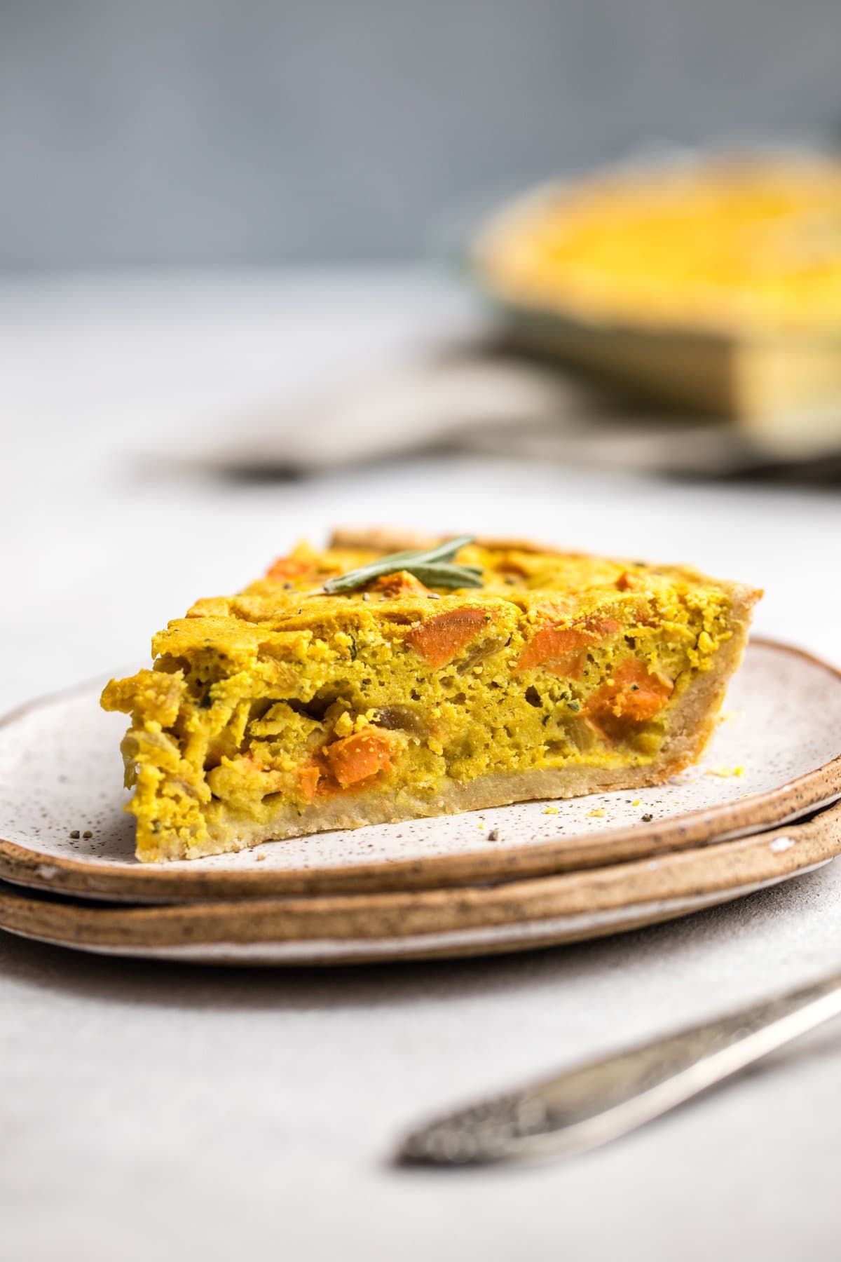 cross section of vegan sweet potato and rosemary quiche on small speckled white plate