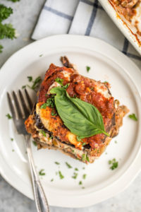 overhead shot of vegan eggplant lasagna topped with fresh basil leaf on small white plate