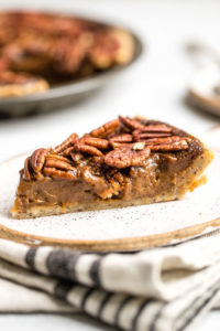 side slice of pecan pie with layers of filling, pecans, and pie crust on white plate