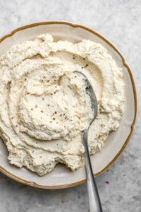 close up of vegan ricotta in tan bowl with silver spoon
