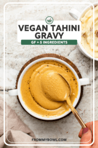 Small white dish of vegan tahini gravy topped with black pepper and a gold serving spoon
