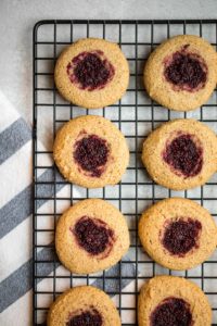 almond flour thumbprint cookies lined up on black wire cooling rack with gray background