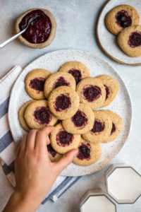 large white plate topped with almond flour thumbprint cookies with hand reaching for a cookie