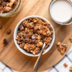 small white bowl filled with chocolate hazelnut granola on round wood cutting board