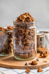 glass jars filled with chocolate hazelnut granola on round wood cutting board