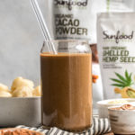 chocolate hemp smoothie in glass with straw with sunfood product in background