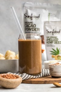 chocolate hemp smoothie in glass with straw with sunfood product in background