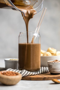 blender pouting chocolate hemp smoothie into tall glass with straw