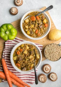 two bowls of curried lentil soup on wooden cutting board with silver spoons