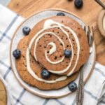 gingerbread pancakes topped with icing swirl on small white plate with blueberries