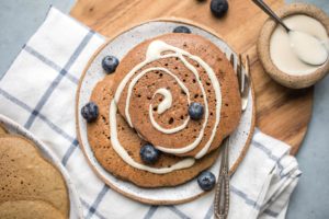 gingerbread pancakes topped with icing swirl on small white plate with blueberries