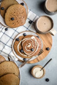 spread of gingerbread pancakes on plates with chai lattes and vegan cream cheese frosting