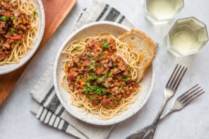 white bowl of spaghetti topped with lentil bolognese and fresh parsley