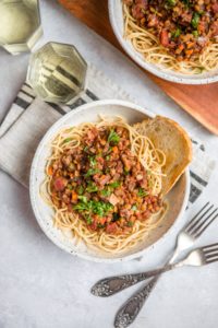 white bowl of cooked pasta topped with lentil bolognese and a glass of white wine