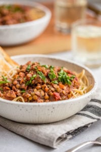 close up photo of Lentil Bolognese sauce over cooked pasta in white bowl topped with fresh parsley