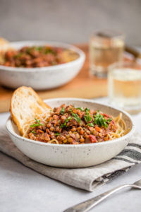 lentil bolognese topped with fresh parsley and garlic bread in speckled white bowl