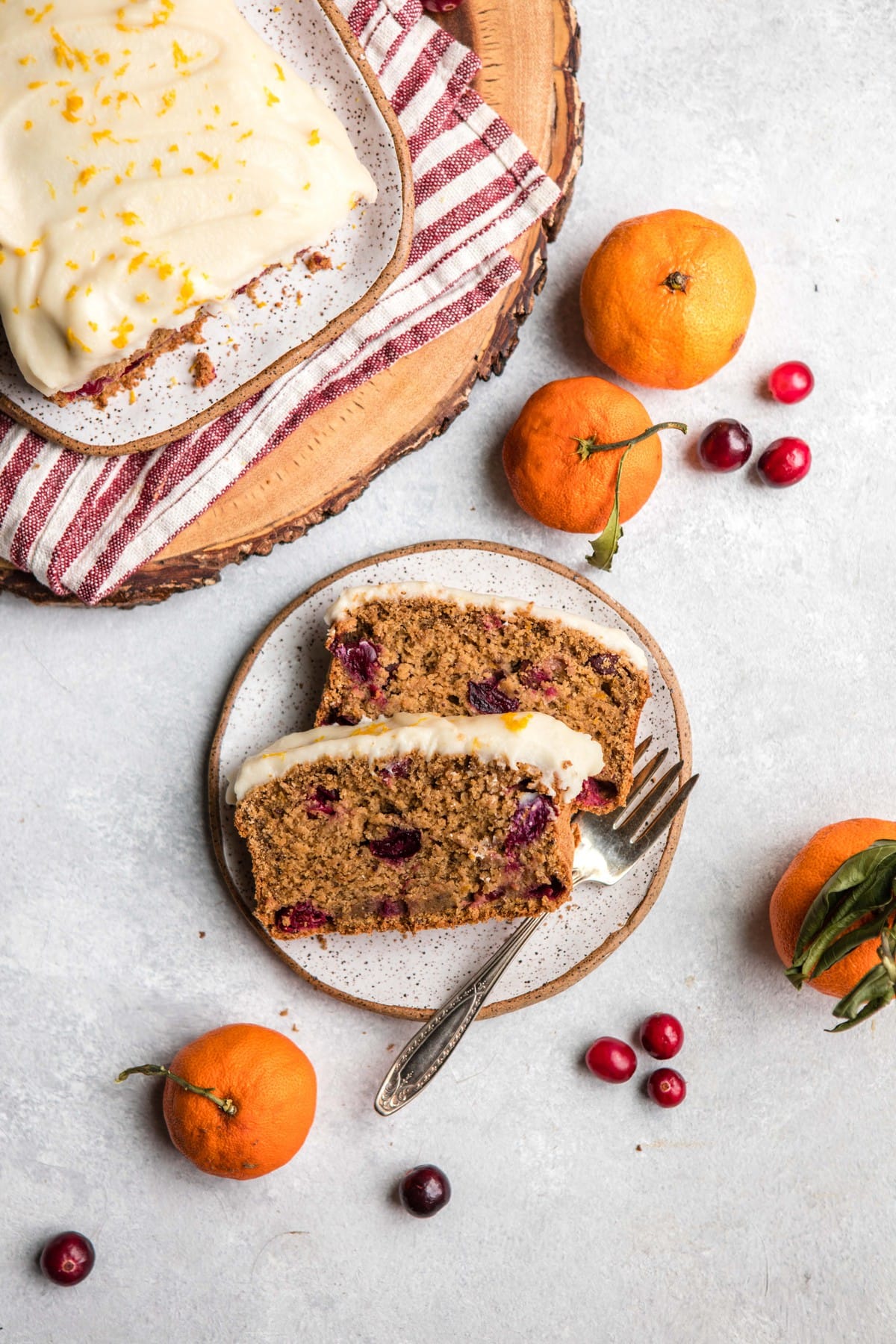 overhead photo of two slices of cranberry orange bread on small white plate with fresh oranges on the side