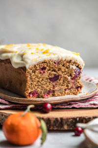 sliced cranberry orange loaf topped with coconut butter glaze on wood serving tray