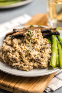close up photo of cooked mushroom risotto on white plate with blanched asaparagus